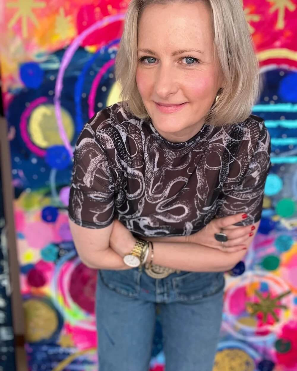 Woman with arms crossed in front of a colorful abstract background